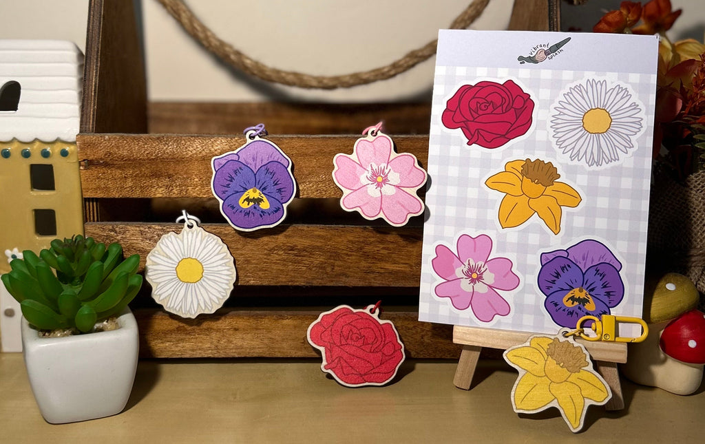 Display of 5 flower shaped wooden keychains and a sticker sheet with the flower designs upon.